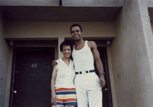 Vel Phillips wearing striped shorts standing next to her son, Dale Phillips. They are standing in front of a doorway.