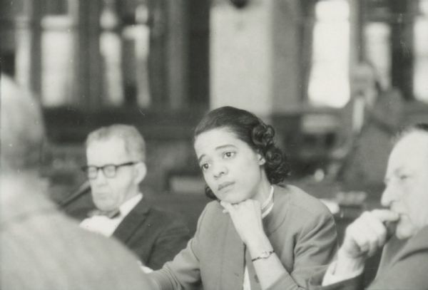 Vel Phillips is sitting in the Milwaukee Common Council chamber. There are two unidentified men sitting next to her.