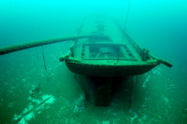 Underwater view of the stern of the schooner <i>Home</i> resting on the bottom of Lake Michigan. One of the masts is broken and is bending over the port side of the ship. The hull appears to be mostly intact.