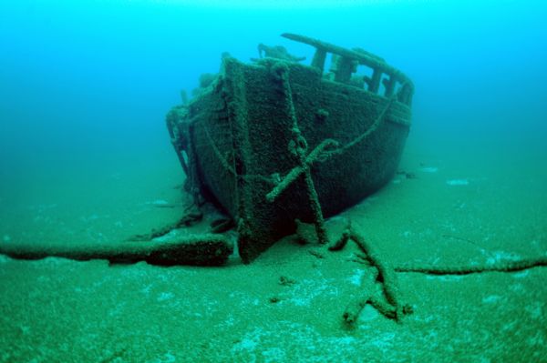 Underwater view of the bow of the schooner <i>Home</i>. The port anchor is hanging along the port side of the ship. The bowsprit is laying on the lake bed on the starboard side. The rest of the ship is sitting upright and remains largely intact.