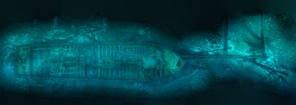 Underwater, overhead view of the wreck of the schooner <i>Rouse Simmons</i> (also known as the Christmas Tree ship). The masts of the schooner are laying on the lake bed near the bow, while other debris surrounds the ship. The planks that make up the deck of the ship are loose and scattered, but the wreck remains largely intact.