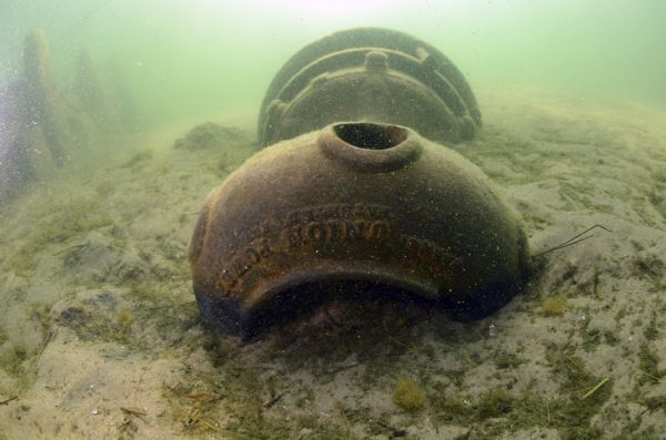 Underwater view of the capstan of the <i>Success</i>. The capstan is laying on its side embedded in the sand, near the stern on the starboard side of the ship. Text on the capstan reads, in part: "Union Power."