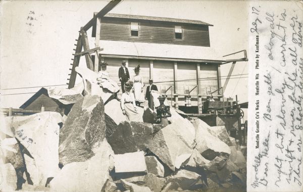 Charles Richter, second from left, poses in front of a building at the top of the Montello granite quarry. His wife stands at the front of the group, wearing a dark blouse and skirt. The other people are unidentified, but two of the girls are likely the Richters' daughters, Ethel May and Blanche. A small cart, a portion of the derrick, and quarry buildings are in the background. The message reads: "Montello, July 17. Dear Helen. Been getting along all right but slowly, current is swift & river bends all over. There are 8 locks besides. Alfred."  The card was sent by Alfred T. Flint (1890-1949) of Madison to his sister Helen. The son of Albert S. and Helen Flint, Alfred Flint was later a Harvard trained attorney. The river referred to in the message is the Fox River. Caption reads: "Montello Granite Co's Works, Montello, Wis."