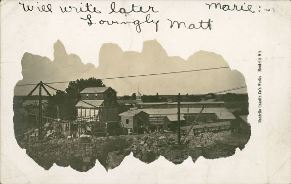 Elevated view looking west over the Montello Granite Company's works framed by an irregular mask. Two wooden derricks and irregular blocks of granite are in the foreground, with the granite company buildings behind. The long building on the right is the quarry's polishing shed. The roof and tower of the Montello House hotel are in the center background, and Buffalo Lake is seen at far left. An elevated narrow gauge railway leads from between two sheds, curving as it extends left towards the lake. A short greeting is handwritten at the top. Caption reads: "Montello Granite Co's Works, Montello, Wis."
