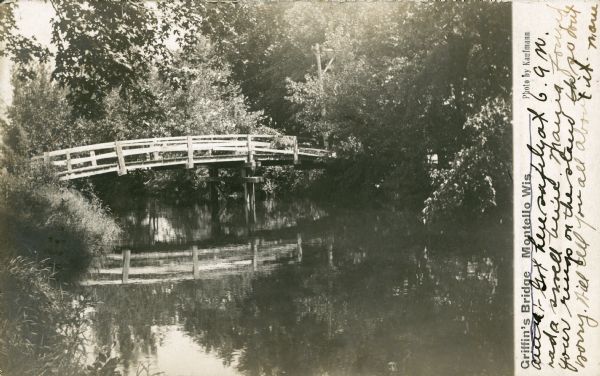 View across water towards a rustic wooden walking bridge which is reflected in the water of the Montello River. There is a utility pole with wires in the background. Caption reads: "Griffin's Bridge, Montello, Wis." The handwritten message reads: "Got here safely at 6 a.m. had a swell time. Maria found your rings on the stand so don't worry. Will tell you all about it. Marie"