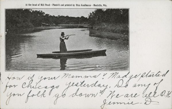 An unidentified woman, wearing a hat and standing in a skiff is aiming a gun toward the shore of the mill pond (Montello Lake). The printed inscription on the front of the card reads: "At the head of Mill Pond — Photo'd and printed by Miss Kaufmann — Montello, Wis." The handwritten message is: "How is your Mamma? Madge started for Chicago yesterday. Do any of you folk go down? We are all O.K. Jennie D —." The card was sent to Miss Marion Kendall, Merrill, Wis.  