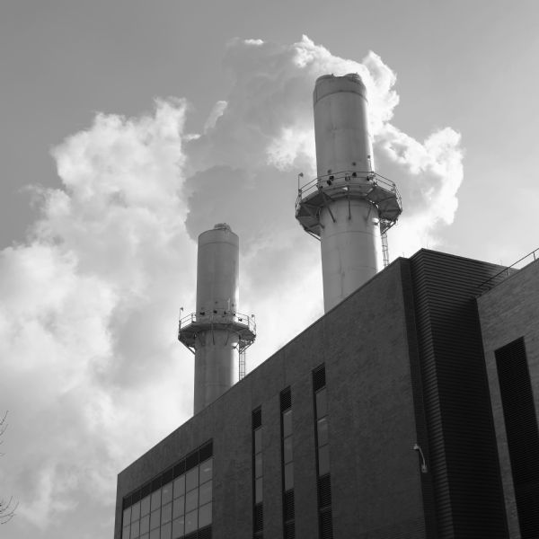 Two smokestacks of a power plant with clouds of exhaust being released into the sky on a cold day. 