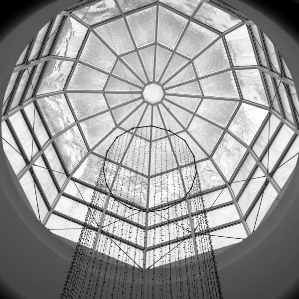 Interior view looking up at the glass dome in the Overture Center. Snow and icicles are on some of the windows of the geometric dome. Suspended below the dome are long strands of decorative lights hanging from a wire support ring.
