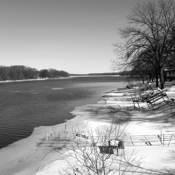 View looking down slope towards ice floes drifting down the Rock River. The steel frame of a dock protrudes from the shoreline on the left, which has a covering of ice and snow.
