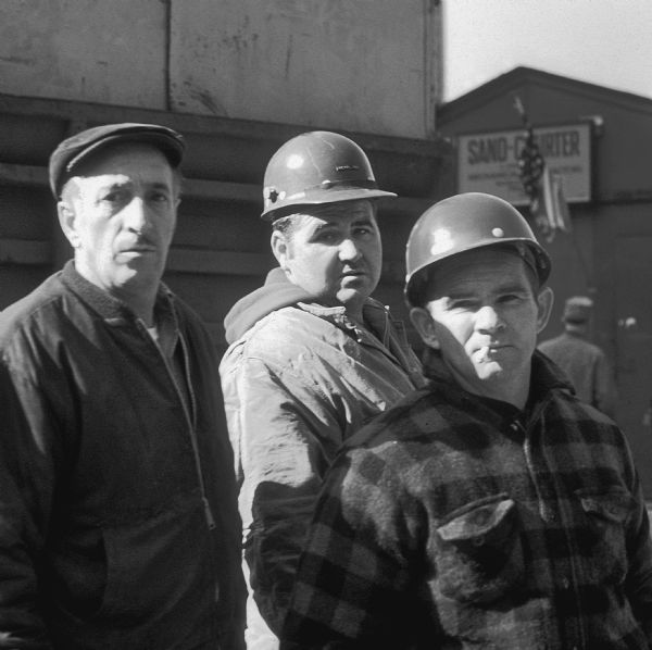 Three construction workers standing near a truck outside the office for the Sand Chapter of Mechanical Contractors at the construction site for the World Trade Center.