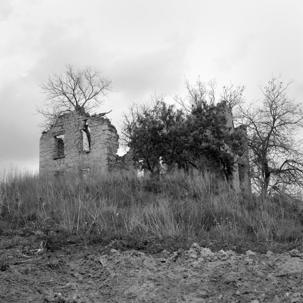 View up hill towards the ruins of a large stone house near Indian Lake. Trees and bushes surround the remains of the building.