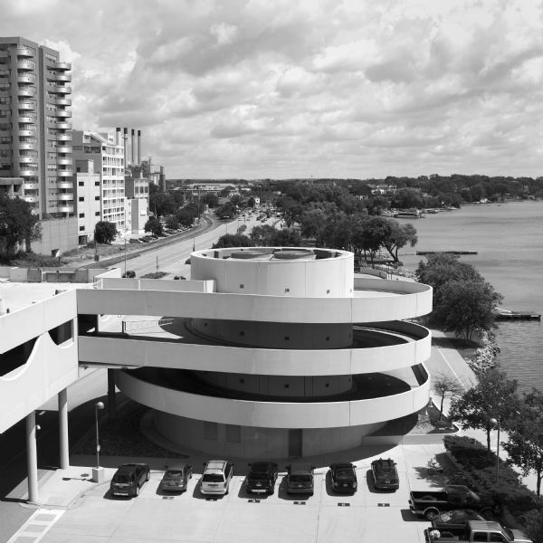 View from the top level of Monona Terrace towards the spiral ramp leading to the outdoor parking lot. Just beyond is John Nolen Drive and railroad tracks. Office, commercial and apartment buildings are on the left. The shoreline of Lake Monona is on the right. 