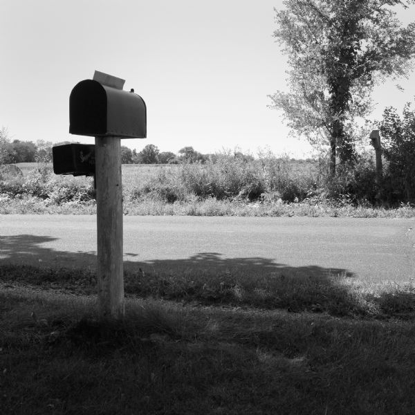 A mailbox near a road. On the other of the road is a field.