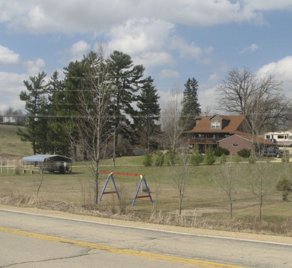 Elevated view across road of a house on Highway 39 between Linden and Mineral Point. There is a swing-set in the yard and a large recreational vehicle parked behind the house.