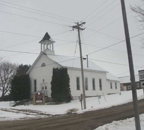 Exterior view of the Waldwick Community Church in wintertime. There are wreaths with red bows on the doors of the church, and snow is on the ground.
