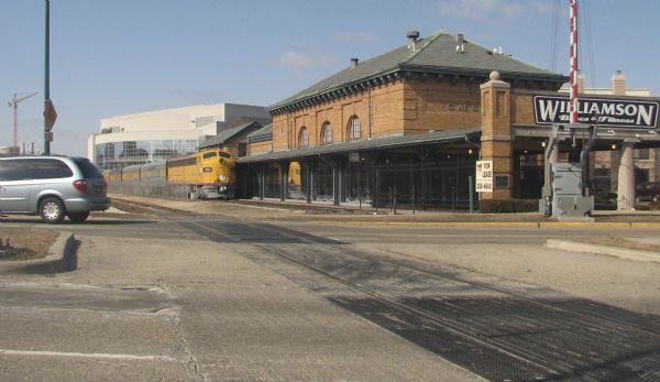 The Historic Train Depot at 640 West Washington Avenue, formerly the site of the Chicago, Milwaukee & St. Paul West Madison Station. There is a train parked on the tracks, and beyond is a sign for Williamson Bikes & Fitness.