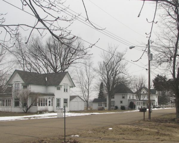 White houses and sparse snow line a street. There is a "Law Office" sign in the foreground.