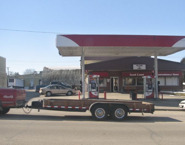 Exterior view of a Cenex filling station, which includes a food court and convenience store. There is a truck with a trailer passing the station in the foreground. This location is the former site of the Blanchardville Depot.