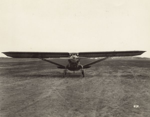 Front view of a Bellanca CH Pacemaker, featuring "flying struts," sitting on a runway. The cantilever axle-type landing gear, an exclusive feature of Bellanca planes, is a principal factor in their sturdiness and safety.
