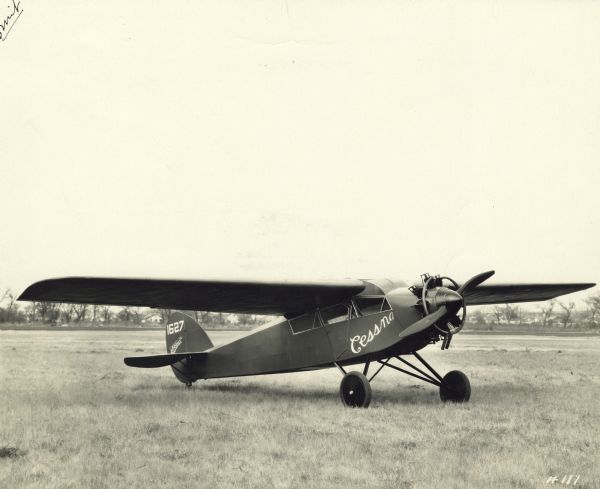 Three-quarter right side view from front of a Cessna Model A aircraft sitting on a runway. The tail identifier reads: "1627." 