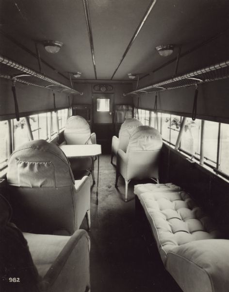 Interior view of a Fokker airplane cabin including five seats, a table, a couch, two cabinets, and overhead storage racks.