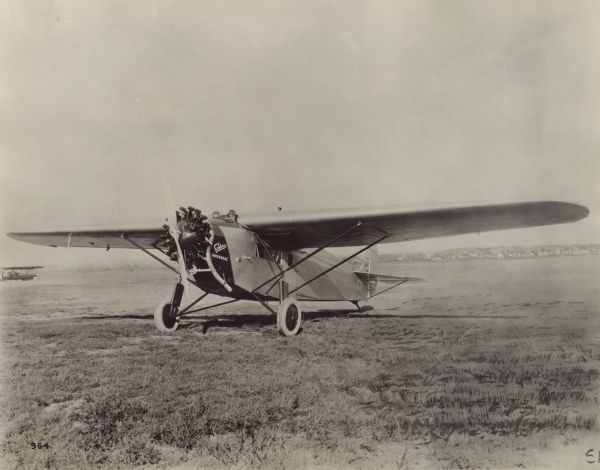 Three-quarter view from front left of a Fokker Universal sitting on a runway. The airplane is powered with a Wright "Whirlwind" 220 hp engine. The pilot and co-pilot are sitting in the double cockpit just forward of the wings.