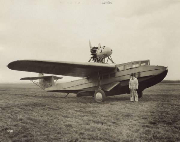 Three-quarter view from front right of a Fokker Amphibian Model F-11 sitting on a runway. A man in Fokker coveralls is standing on the ground next to the plane.