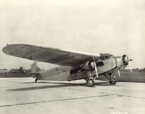 Three-quarter view from front right of a Ford 4-AT-B Trimotor sitting on a runway. The airplane is equipped with three 220 hp Wright J-5 engines, and has a wing span of 74 ft. It stands 12 ft high and has a length of 49 ft, 10 in. The tail identifier reads: "7117."