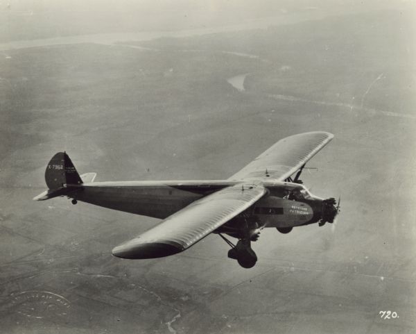 Aerial view looking down at a Keystone K-78 "Patrician" in flight. The "Patrician" is a twenty-passenger monoplane powered by three Wright Cyclone engines. Fields and rivers are below.