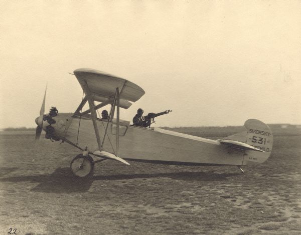 Right side view of a Sikorsky S-31, equipped with a 200hp Wright J-4 engine, sitting on a runway. These models were bought by Fairchild Co. to be used for aerial photography. However, in this photograph, the second open cockpit is occupied by a man with a machine gun. The pilot is sitting in the front open cockpit.