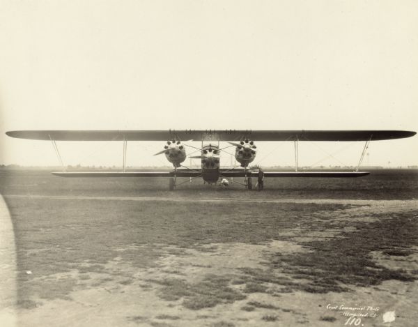 Front view of a Sikorsky S-35 sitting on a runway. The S-35 is powered by three 420 hp Gnôme-Rhône Jupiter engines. Two men are working on the plane: one is standing in front of the plane near the far right engine, and another man is crouching behind the airplane near the tail.