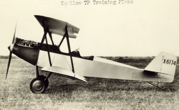 Left side view of a Swallow TP (training plane) sitting on a runway. The tail identifier reads: "X6174." The Swallow TP biplane was equipped with a Curtiss OX-5 engine. It was often used to train new pilots as it was fairly simple to fly and maintain.