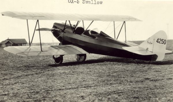Three-quarter view from left rear of a OX-5 Swallow sitting on a runway. The tail identifier reads: "4250." This airplane was powered by a Curtiss OX-5 eight-cylinder V-8 engine. 