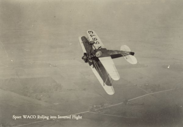 Aerial view of a WACO ATO (also known as a 10-T Taperwing) rolling into inverted flight. The wing identifier reads: "5673." The airplane is powered by a 220hp Wright J-5 motor.