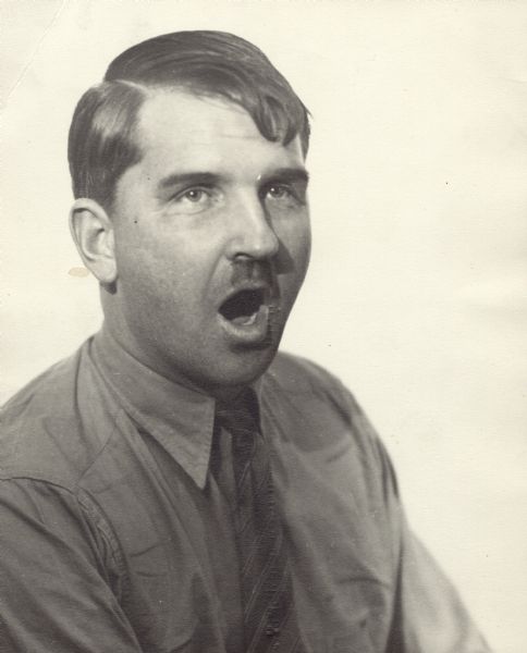 Portrait of Sid Boyum with his mouth open as if speaking. He is dressed as Adolf Hitler and has a fake moustache.