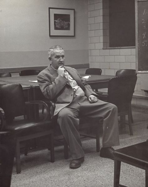 Portrait of Sid, wearing a suit and sitting in a chair in a Gisholt conference room with his hand on his chin.