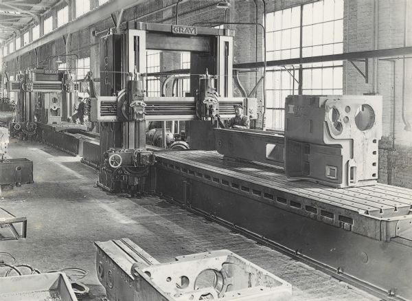 Interior view of Gisholt Machine Company. Two men are standing next to large machinery, marked with the name "GRAY."