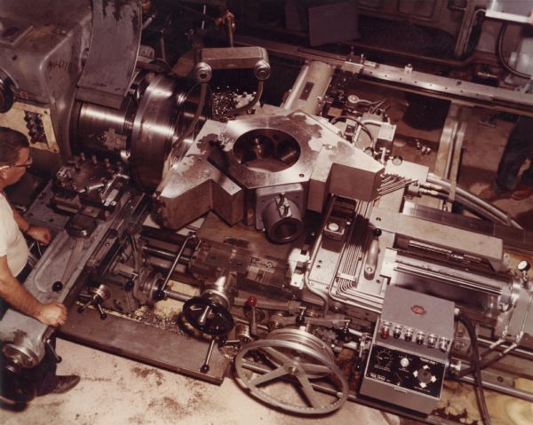 Elevated view of a milling machine inside the Gisholt Machine Company. A male employee on the left is working with the machine.