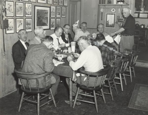 Group of Ducks Unlimited group members, including Sid Boyum with his arm in the air, sitting at a large table in the Cherokee Cabin hunting lodge located in what is now Cherokee Marsh.  Stan Johnson (Hobart Stanley Johnson Jr.) is standing.