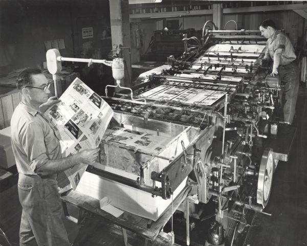 Elevated view of two employees running the internal printing press of Gisholt Machine Company. They are printing product pamphlets.