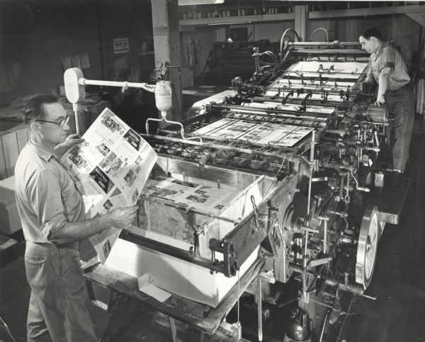 Elevated view of two employees running the internal printing press of Gisholt Machine Company. They are printing product pamphlets. 