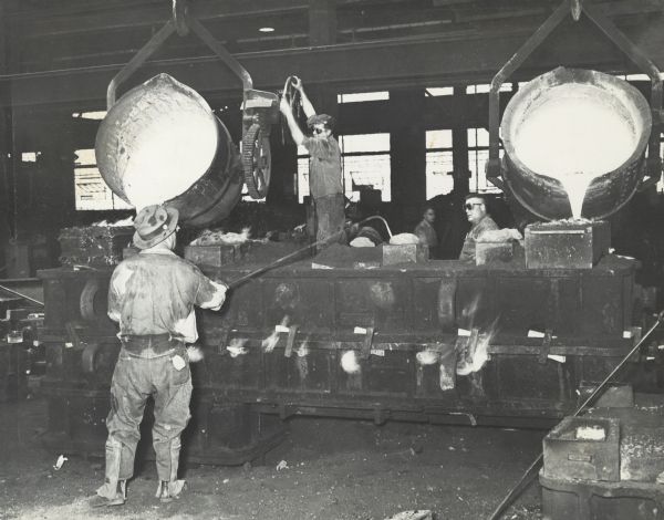 Workers pouring liquid metal from large cauldrons at the Gisholt Machine Company foundry.