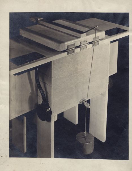 Contact printer in closed position with suspended weight laced through pulley. This printer was in the photography lab at Gisholt Machine Company, when Sid Boyum was employed as the industrial and engineering photographer. The photographic print was made circa 1950s or 1960s.