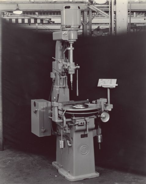 Drill press and static balancer set up in front of a dark backdrop. The factory ceiling is in the upper background. A plate on the front of the balancer reads: "Gisholt Static Balancer."
