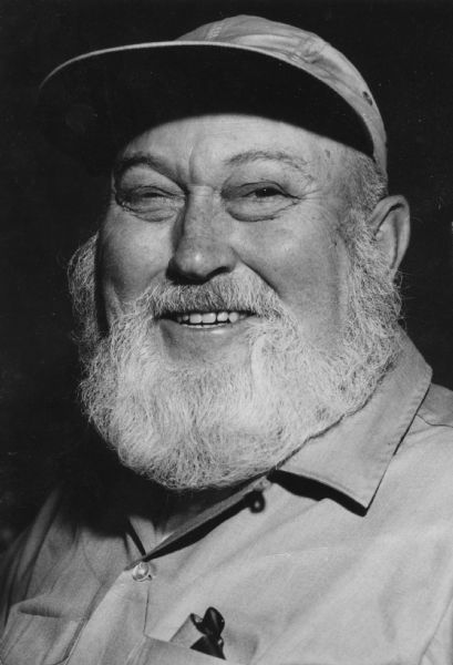 Head shot of an older man with a white beard. He wears a cap  and what looks like a work shirt and is probably a Gisholt employee.
