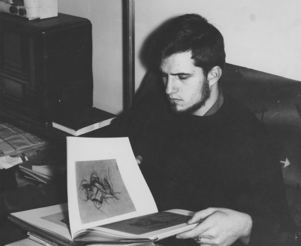 Steve sitting on a couch and reviewing the illustrations in a drawing book. 