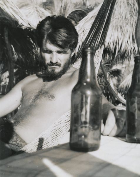 Steve, Sid Boyum's son, sitting in a hammock. Two bottles of beer are on the table in the foreground.