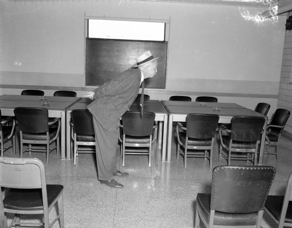 Side view of Sid bending over and posing in a meeting room of Gisholt.
