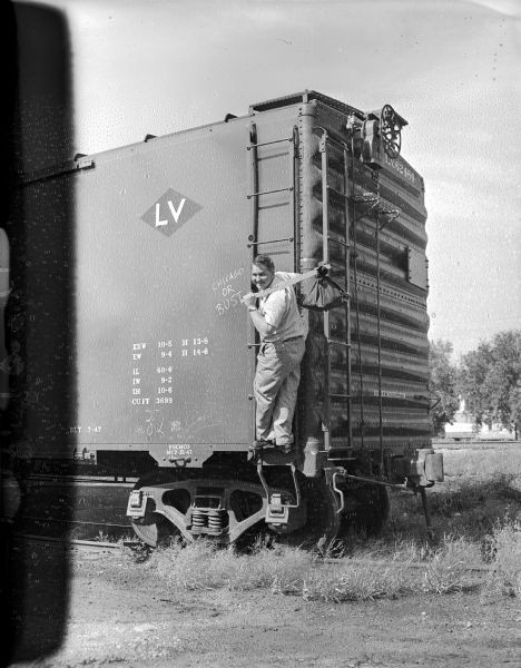 Sid posing as a hobo, standing on a ladder on the back of a box car. He is wearing a wristwatch, and is looking over his left shoulder and carrying a bindle. Written on the side of the car next to the ladder: "Chicago or Bust."