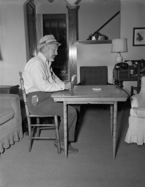 View of a man playing poker alone on the left side of a table in a living room. In the background is a stairwell.